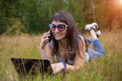 Portrait of smiling young woman using mobile phone while standing against plants