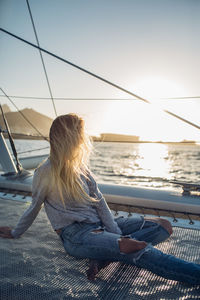 Woman sitting in sea against sky during sunset