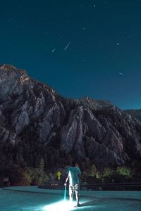 Rear view of man standing on mountain against sea at night