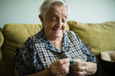 Portrait of smiling senior woman crocheting on the couch at home