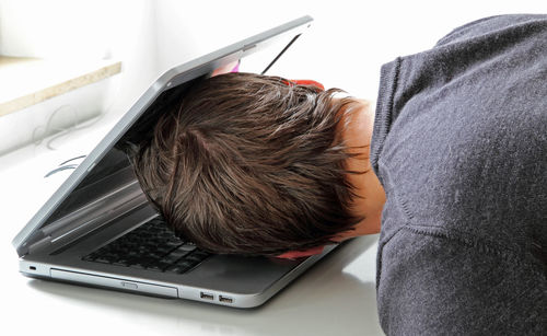 Side view of man laying on laptop at desk