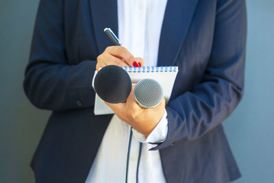 Female journalist at news conference or media event, writing notes, holding microphone