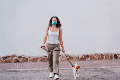 Full length of woman with dog walking against wall