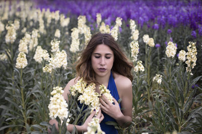 Beautiful young woman with eyes closed sitting amidst flowers on field
