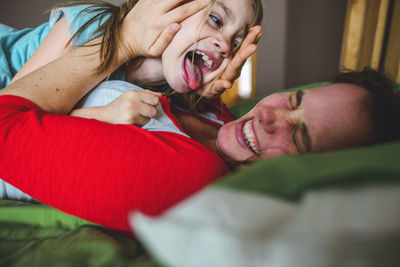 Side view of playful daughter licking mother lying on bed at home