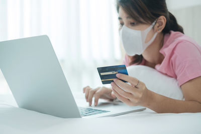 Side view of woman wearing mask using laptop at home