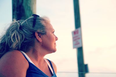 Low angle view of thoughtful mature woman looking away while sitting against sky