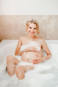High angle portrait of naked pregnant woman covering breasts while taking a bath in bathtub
