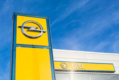 Low angle view of yellow sign against blue sky