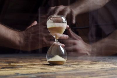 Blurred motion of people holding hourglass on wooden table