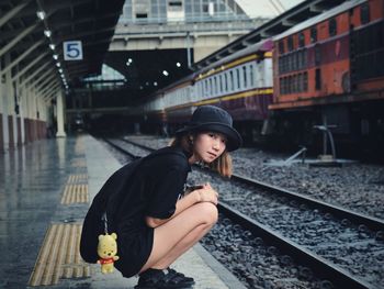 Portrait of woman crouching at railroad station platform in city