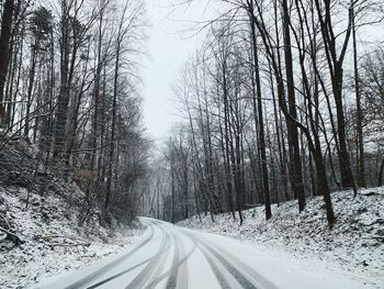 Snow covered road amidst trees during winter