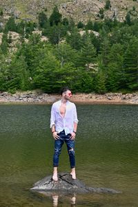Full length of young man standing in lake against trees