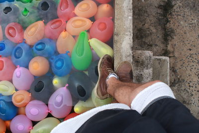 Low section of man standing on swimming pool with colorful water balloons