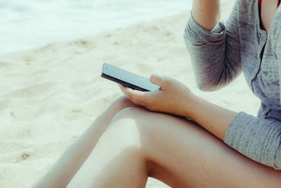 Midsection of woman using mobile phone while sitting at beach