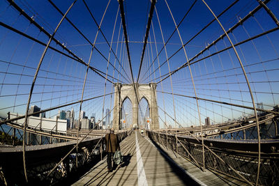 Rear view of man walking on bridge against blue sky