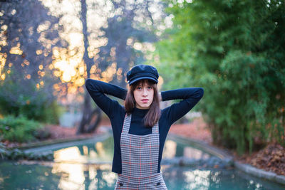 Portrait of young woman standing by swimming pool against trees