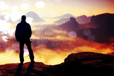 Silhouette man standing on rock against sky during sunset