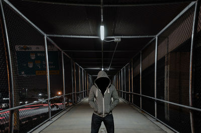 Person wearing hooded shirt standing on footbridge at night