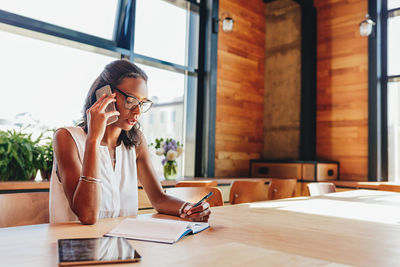 Woman using phone while sitting on table