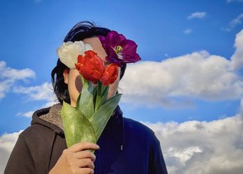 Young man holding bunch of tulips against white clouds in blue sky.