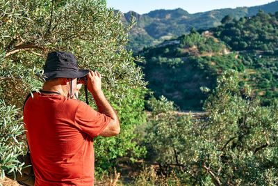 Rear view of tourist man looking through binoculars at the mountains view. hiking, unity with nature