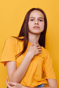 Portrait of young woman sitting against yellow background