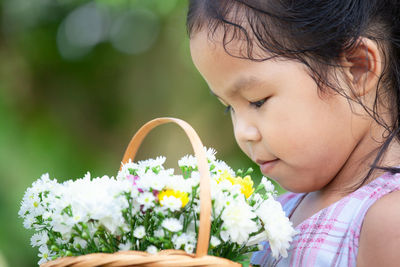 Close-up of cute girl looking at basket with flowers while standing in yard
