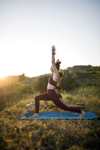 Women practicing yoga on mats against clear sky at sunset