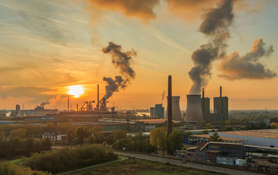 Smoke emitting from factory against sky during sunset