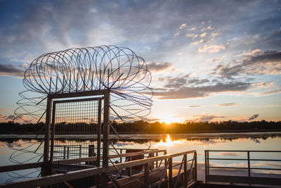 Silhouette ferris wheel by lake against sky during sunset