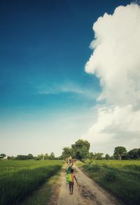 Rear view of woman and child walking on dirt road against sky