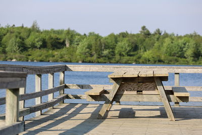 Empty deck chairs by lake against sky