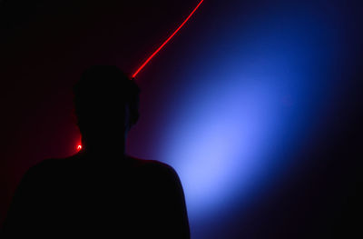 Rear view of silhouette man standing against illuminated wall