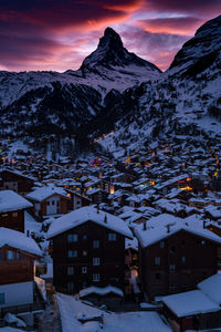 Houses and snowcapped mountains against sky during winter