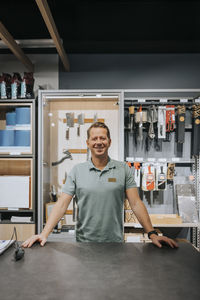 Portrait of smiling mature male sales clerk standing at checkout counter in appliances store