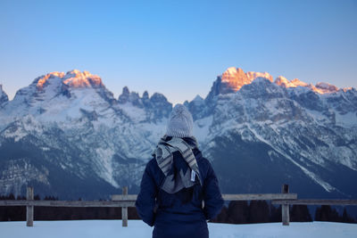 Woman standing on snowcapped mountain against clear blue sky