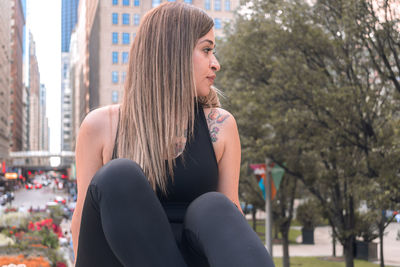 Young woman looking away while sitting on tree