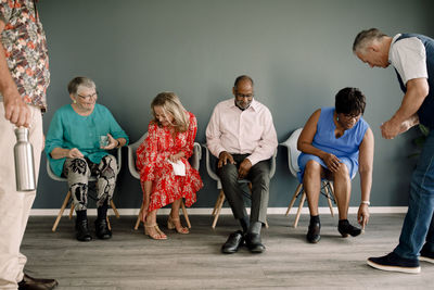 Senior women and men wearing footwear while sitting on chairs by male friends in dance class