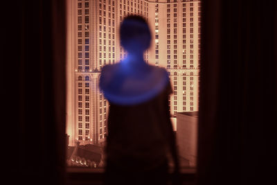 Rear view of silhouette woman looking through window while standing in darkroom