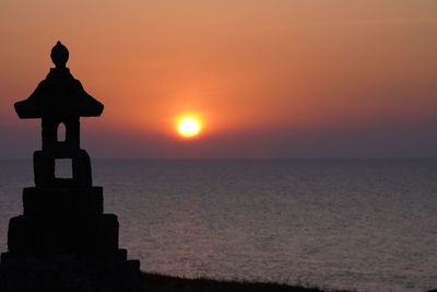 Silhouette cross on sea against sky during sunset