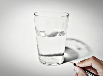 Person holding pencil by glass of drinking water