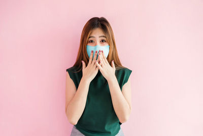 Portrait of young woman standing against pink background