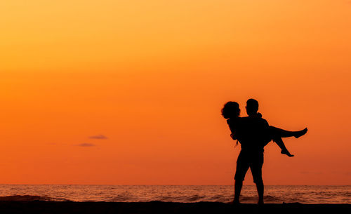 Couple at beach, silhouette in sunset, love and friendship, man lifting woman.