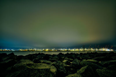 Rocks at sea shore against sky at night