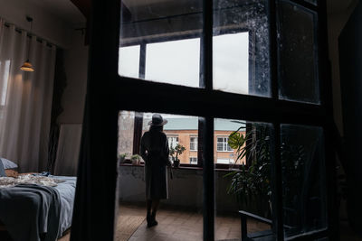 Silhouette of a woman in a beige autumn coat and hat on the background of the window