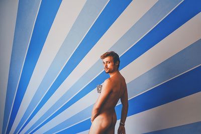 Portrait of naked young man standing against wall