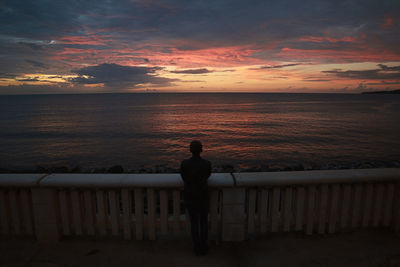 Silhouette man looking at sea against sky during sunset