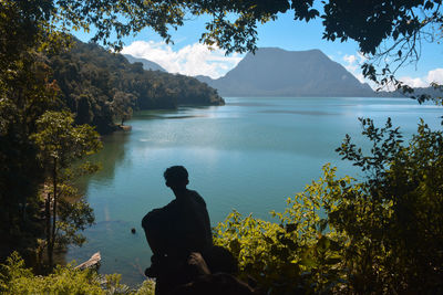 Side view of silhouette man looking at lake by mountain