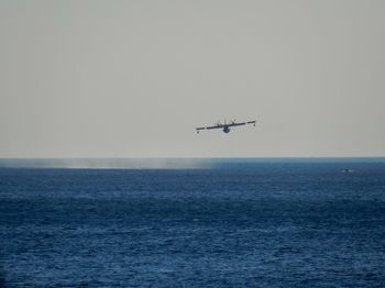 Airplane flying over sea against clear sky